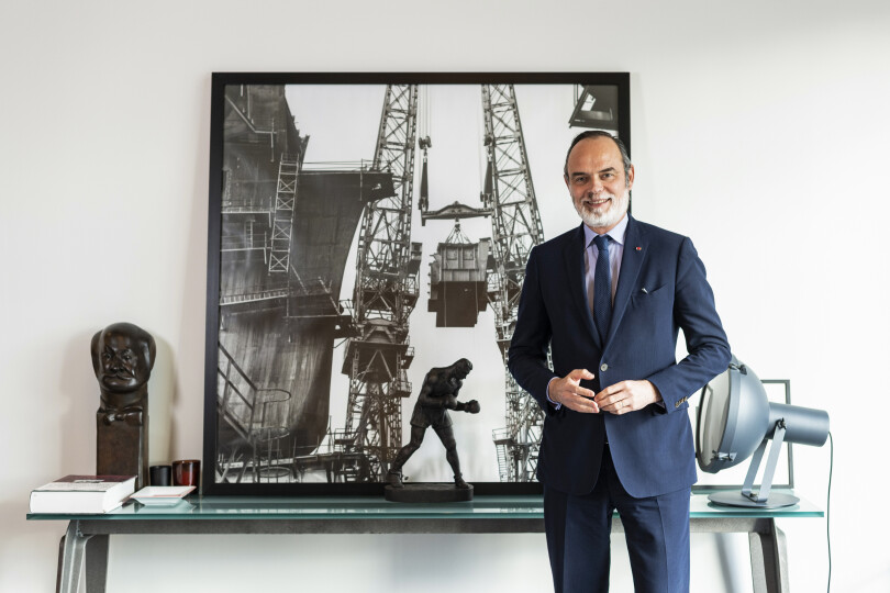 Le maire du Havre pose dans son bureau. Derrière lui, une photo du port de la ville.